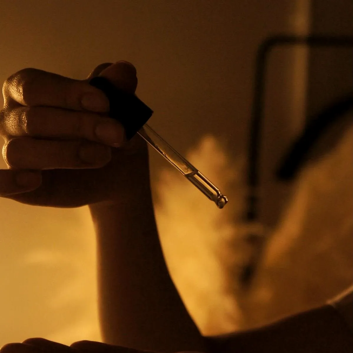 Facial serum from a glass dropper held over an open palm, with warm steam behind, at Millán Spa