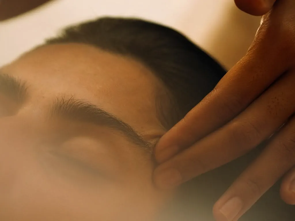 A therapist massaging a client's temples over warm steam during a facial at Millán Spa