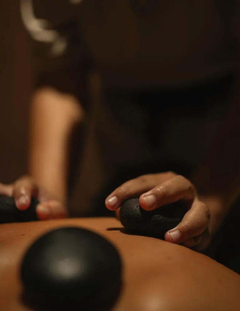 A therapist's hands working a client's back with warm stones
