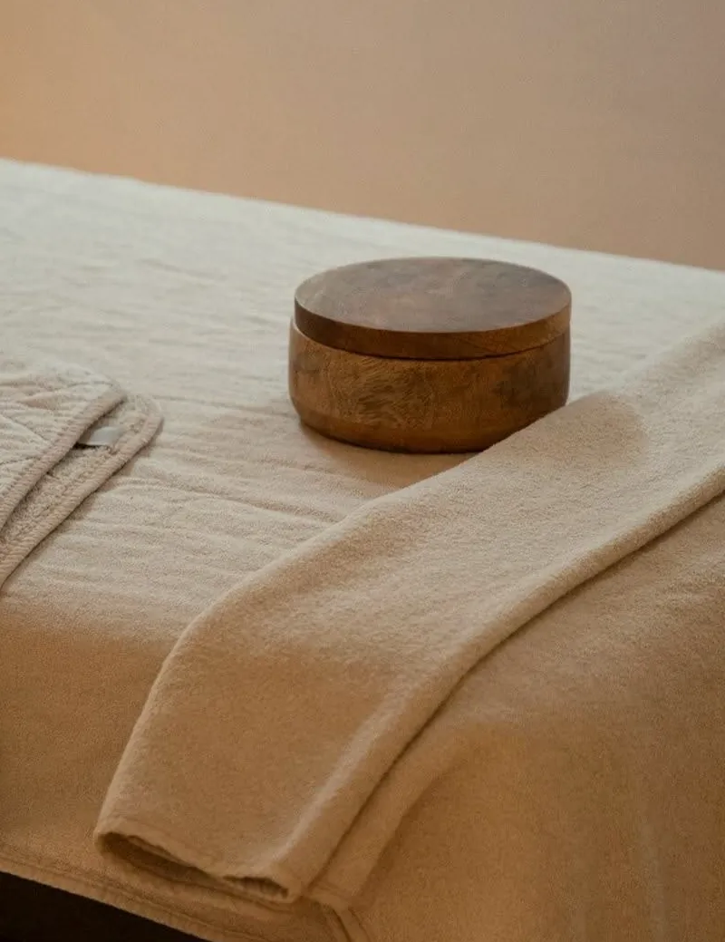 A massage table dressed in linen with a wooden bowl, ready for the next session