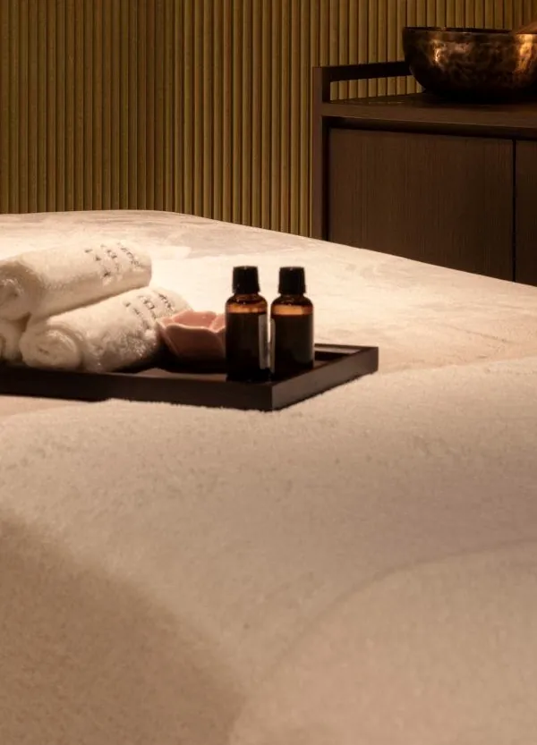 Rolled white towels and a tray of facial oils on a linen-dressed treatment table at Millán Spa