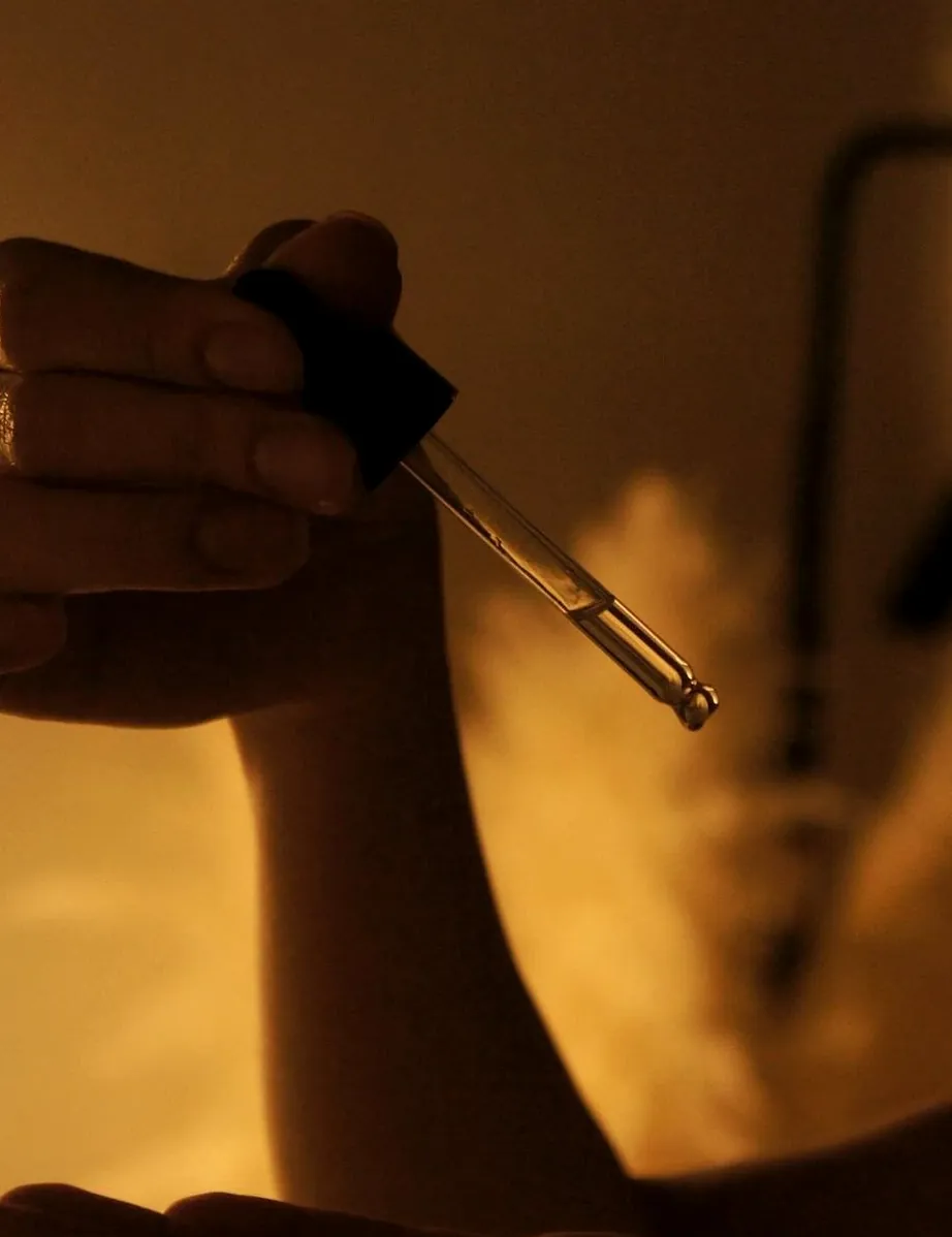 A glass dropper of serum over an open palm, in warm light